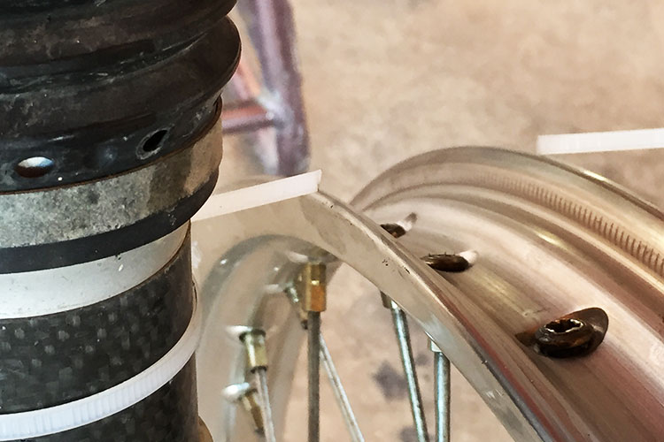 You do not need a wheel stand to true the rim up. You can mount the wheel on the bike and use the fork leg or the swingarm to attach zip-ties that will act as guides to show you if the rim is straight and true. 